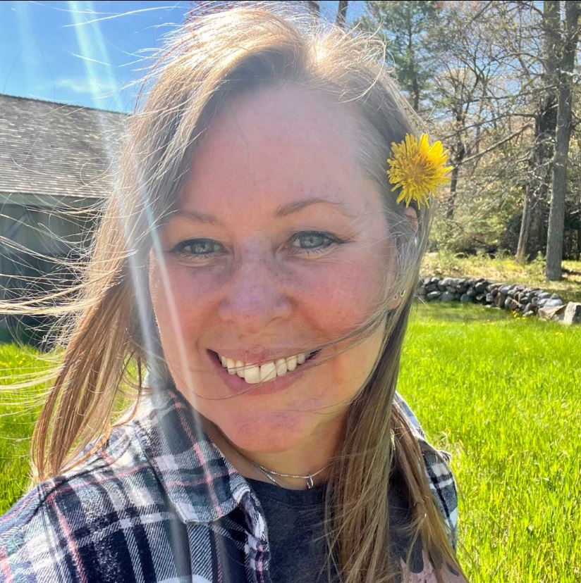 Community herbalist Leanne Shafner of Lioness Wellness & Aromatics, smiling outdoors with a dandelion in her hair